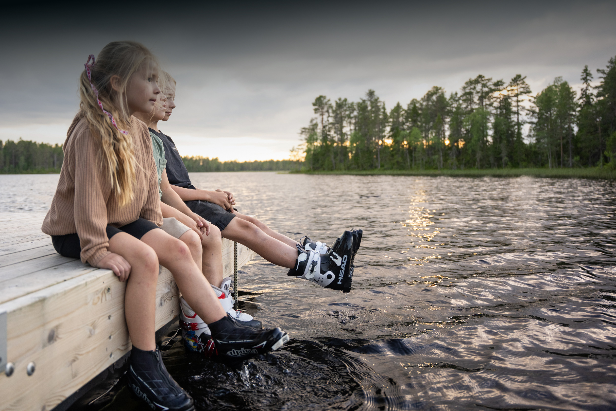 Barn sitter på en brygga med fötterna i vattnet vid en sjö.