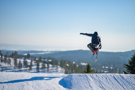 Skidåkare gör ett hopp i en snowpark med snölandskap och skog i bakgrunden.