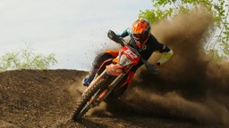 Motocrossförare i orange hjälm kör i hög fart genom en kurva, med jord som yr upp bakom motorcykeln.