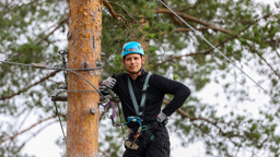 Man i klätterpark med sele vid träd ger tummen upp